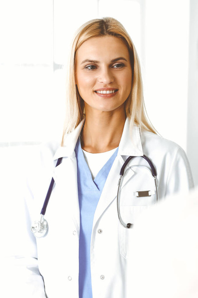 Woman-doctor at work in hospital is happy to communicate with female patient. Blonde physician checks medical history record and exam results. Medicine concept - Photo, Image