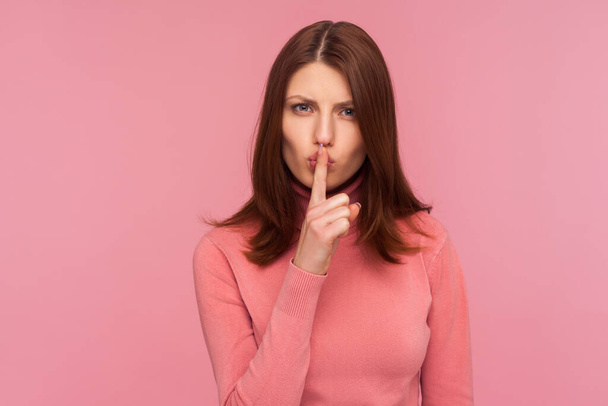 Serious concerned brunette woman showing shh gesture holding finger near lips, keep silence, dont speak. Indoor studio shot isolated on pink background - Фото, изображение