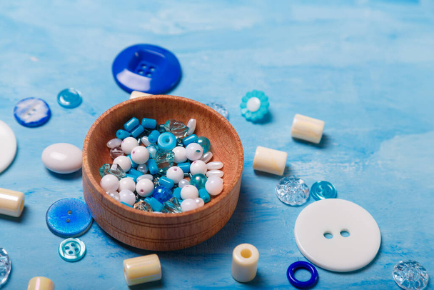 Close up of wooden bowl of beads and buttons for sewing and embroidery. Set of materials for handcraft, making of bijouterie and accessories. Blue background, copy space. - Photo, Image