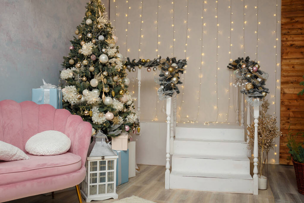 Noel ve yeni yıl kutlaması için dekore edilmiş bir oda. Pembe kanepe, köknar ağacı ve beyaz merdivenler. Tatil ruhu. Modern iç mimari. - Fotoğraf, Görsel