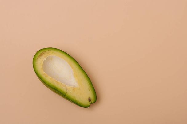 One half of green fresh avocado without seed on beige background. Minimal styled composition. - Fotografie, Obrázek