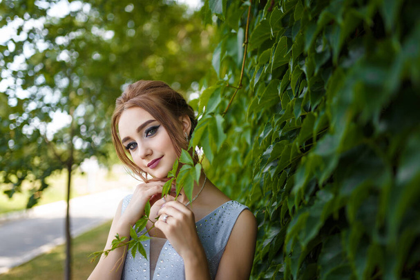 Piękna dziewczyna w przetargu sukienka balowa na zielonym tle bluszcz krzak. Portret kobiety na wiosennym krajobrazie. - Zdjęcie, obraz