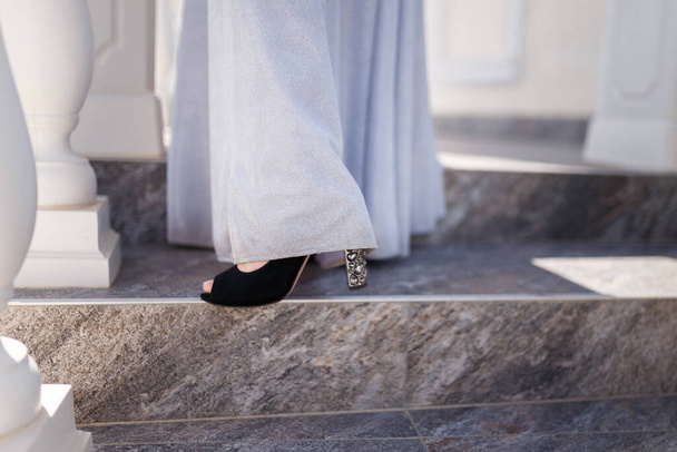 Beaux pieds féminins en chaussures brillantes à talons hauts avec une longue robe blanche tendre. Accessoires pour décrocheuses ou mariées et concept de vêtements féminins. - Photo, image