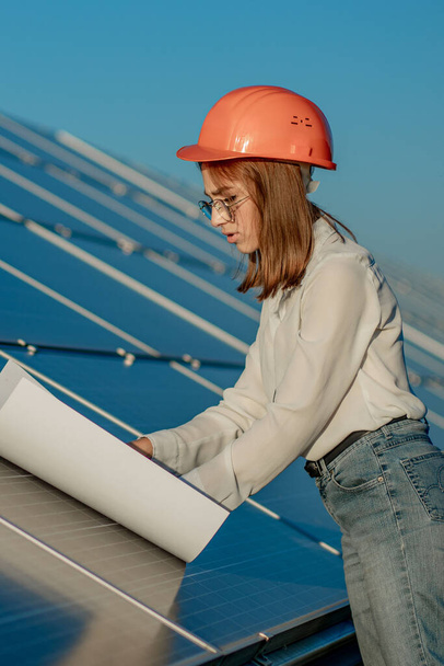 Handsome Architect Woman Examining a Draft Map or Blueprint Project Plan, Worker Activity Looking Out in Photovoltaic Cell Farm or Solar Panels Field. - Foto, afbeelding