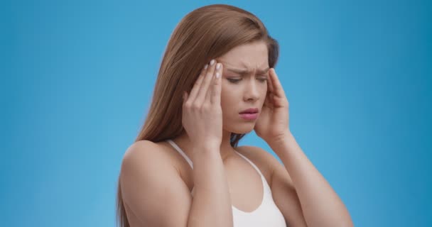 Ostry ból głowy. świątynie, cierpiące na atak migreny, niebieskie tło studio - Materiał filmowy, wideo