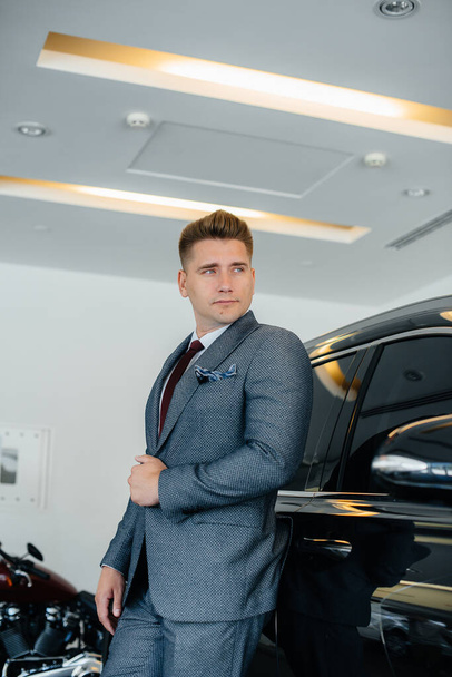 A young businessman looks at a new car in a car dealership. Buying a car - Zdjęcie, obraz