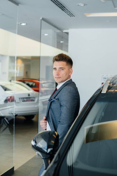 A young businessman looks at a new car in a car dealership. Buying a car - Foto, Imagem