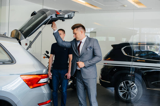 Ein junger Geschäftsmann untersucht mit einem Verkäufer den Kofferraum eines Neuwagens in einem Autohaus. Autokauf - Foto, Bild