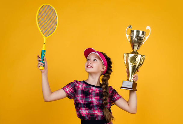 winner child with racquet and champions cup. teen girl win tennis championship. sport. tennis or badminton player. healthy and active lifestyle. full of energy. happy childhood. kid hold racket - Foto, afbeelding