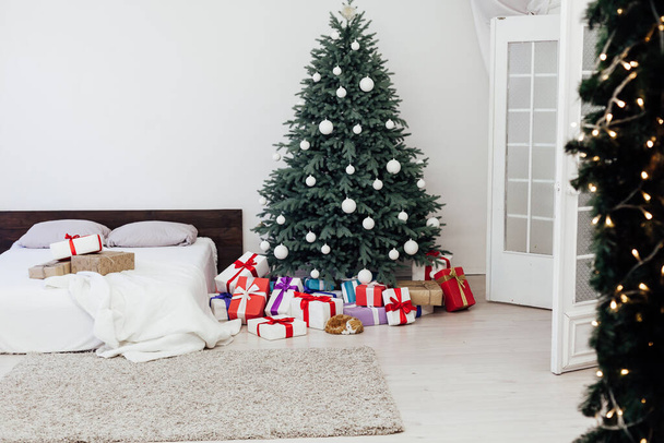 Kerstboom met geschenken in de slaapkamer bed bloemenslingers het nieuwe jaar interieur - Foto, afbeelding