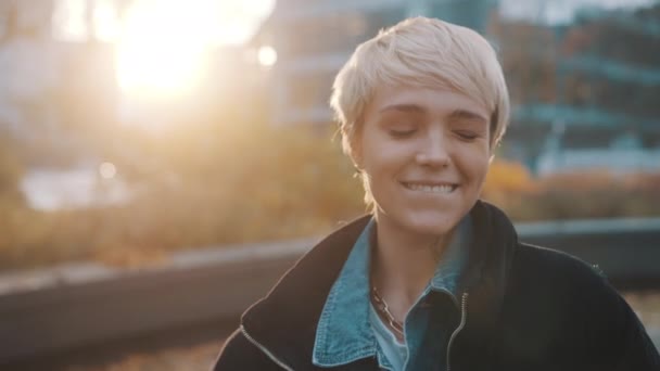 Portrét mladé bělošky s krátkými blond vlasy mrkajícími v městském parku - Záběry, video