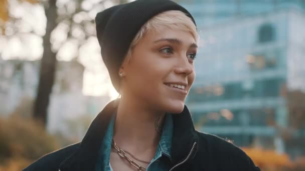 Portrét mladé usměvavé ženy s černým kloboukem a zimní bundou ve městě  - Záběry, video