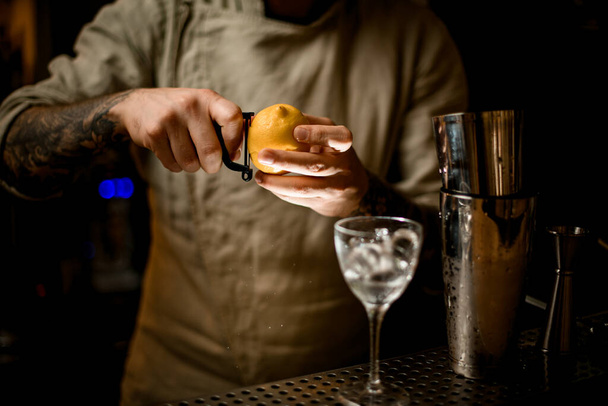 bartender holds lemon in his hands and cuts the peel off with knife - Fotografie, Obrázek