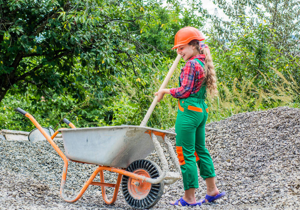 Future profession. future engineer. happy kid use construction wheelbarrow. building construction site. child architect worker. labor day concept. childhood development. teenager girl assistant - Foto, afbeelding