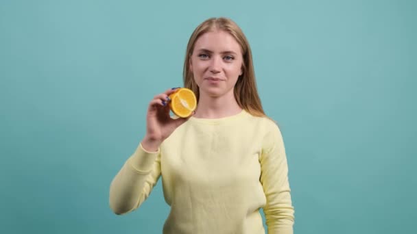 Αστείο χαρούμενο κορίτσι που κρατάει το μισό πορτοκάλι στο στόμα της. - Πλάνα, βίντεο