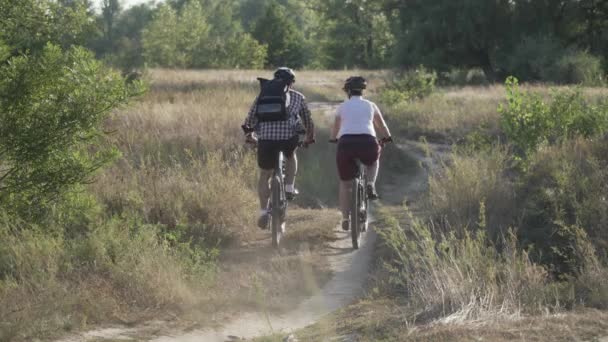 Man and woman ride mountain bikes together on rural road in nature summer, sunny weather. Couple cyclists spend active time exercising outdoor. Family sports biking weekend. People, leisure lifestyle - Footage, Video
