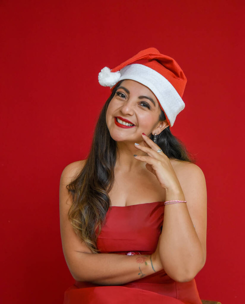 latin woman with red background and celebrating christmas, smiling and happy enjoying the party, merry christmas, red background an piata - Photo, Image