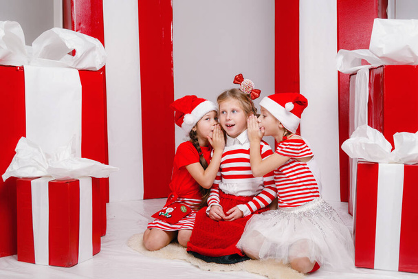 drôles de petites copines en costumes de Noël sur fond de grands cadeaux rouges. idée et concept de vacances heureuses, nouvelle année, amitié et enfance. - Photo, image