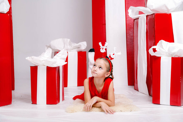 happy funny child girl in Christmas costume with big red gifts on background. - Foto, imagen
