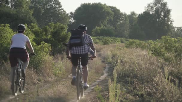 Kırsalda bisiklete binen mutlu çift. Fitness, spor, insanlar ve sağlıklı yaşam tarzı konsepti. Kırsal kesimde tatil bisikleti. Aktif çift bisikletçiler manzaralı yolda dağ bisikleti sürerler - Video, Çekim