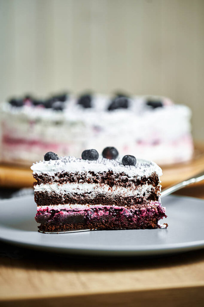 Slice of cake with berries on plate. Board with delicious tasty homemade cake on table. Wooden background - Photo, image