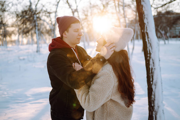 Young couple on winter holiday in a snowy forest at sunset. Handsome young man embracing his girlfriend in a winter day. People, season, travel, love and leisure concept. - Photo, image