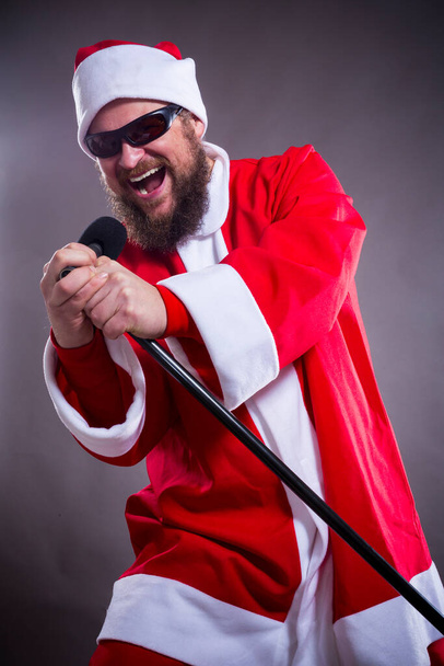 Bearded rocke with micriphome dressed in Santa Claus costume - 写真・画像