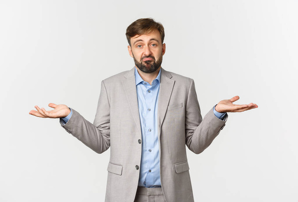Portrait of sad businessman in grey suit, shrugging and looking puzzled, dont know anything, standing confused over white background - Photo, Image