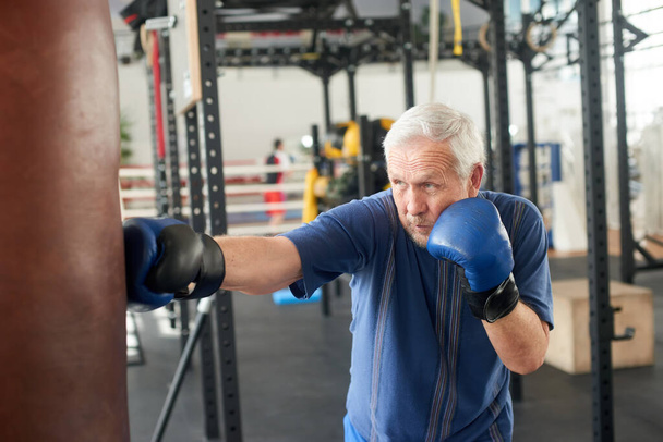 Senior man hitting punching bag in boxing studio. - Photo, Image