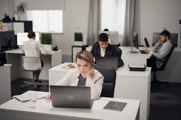 Una joven gerente en la oficina en un código de vestimenta de trabajo con un ordenador portátil se comunica con un cliente de la empresa. - Foto, imagen