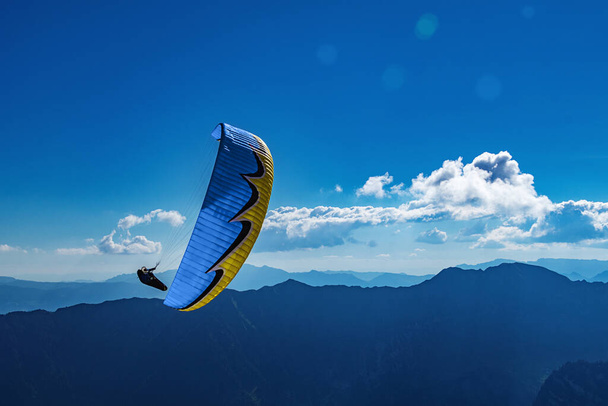 El parapente amarillo-azul vuela en el cielo azul sobre el fondo de las montañas. Parapente en el cielo en un día soleado. - Foto, Imagen