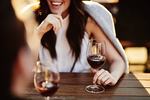Güzel, gülümseyen bir kız bir kafede, bir masada arkadaşıyla oturuyor ve şarap içiyor. - Fotoğraf, Görsel