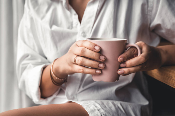 Woman in a white t-shirt holds morning coffee in a pink ceramic cup. Manicure.  - Foto, imagen