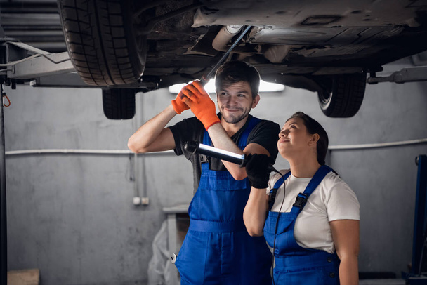 Vrouw en monteur inspecteren auto met zaklamp - Foto, afbeelding