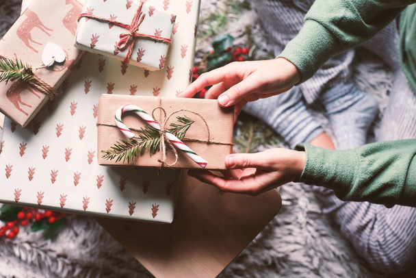 Scène de Noël sur un tapis avec gui et cadeaux enveloppés dans du papier écologique. Une personne en vêtements confortables prend un cadeau. - Photo, image