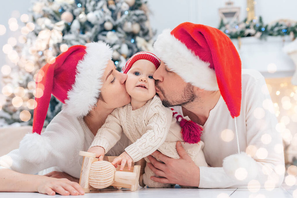Happy family under Christmas tree. baby boy in Santa Claus hat with gifts under Christmas tree with many gift boxes presents. Happy Holidays, New year. Cozy warm winter evening at home. Xmas time - Фото, зображення