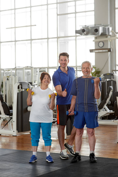Portrait of happy senior couple with trainer at gym. - Photo, Image