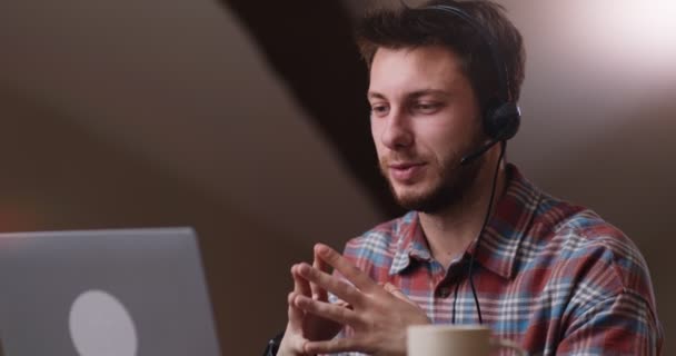 Zelfverzekerde man draagt headset in gesprek op videoconferentie online, legt project uit met gebaren op afgelegen werkplek - Video