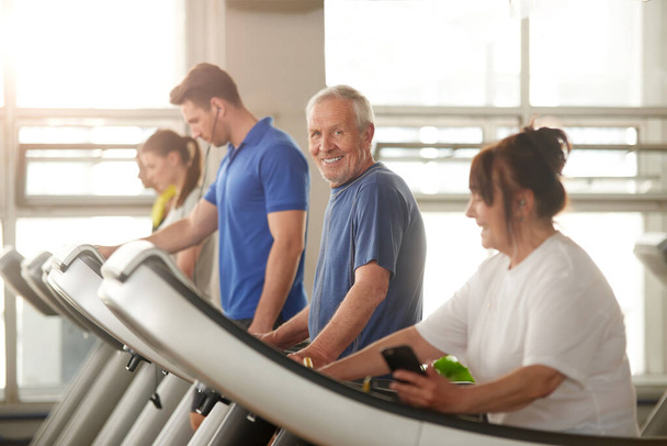 Old happy man runs on treadmill. - Foto, afbeelding
