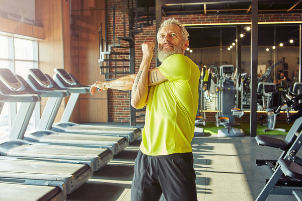Sportos középkorú férfi portréja sportruhában, ahogy nyújtózkodik, felmelegszik edzés előtt egy edzőteremben vagy sportklubban. - Fotó, kép