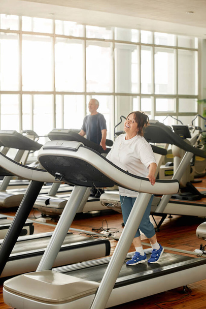 Happy senior woman in earphones exercising at gym. - Photo, Image