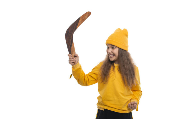 黄色のトラックスーツとニット帽を着て白い背景にブーメランを演奏する若い笑顔の少女の半分の長さの肖像画。健康的なライフスタイルのコンセプト. - 写真・画像