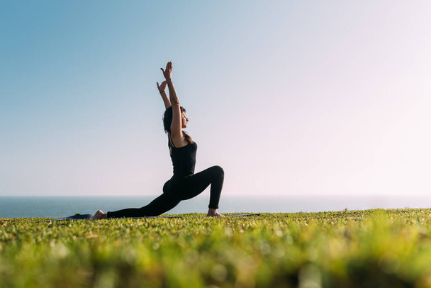 Slim woman in black stretches her body in yoga practice outdoors. Copy space - Photo, Image