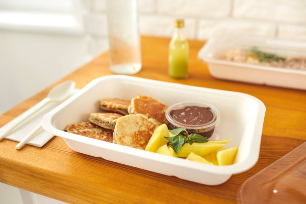 Healthy delicious dessert of pancakes with chocolate pudding and sliced fruit in takeaway container - 写真・画像
