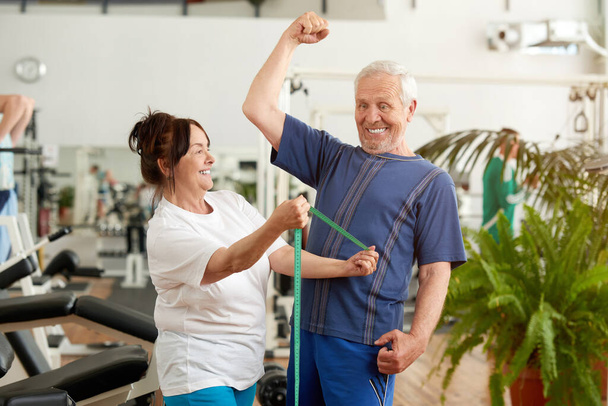 Divertido hombre mayor flexionando sus músculos en el gimnasio. - Foto, imagen