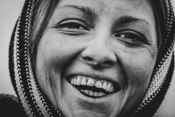 Ασπρόμαυρη φωτογραφία ενός χαμογελαστού βρώμικου γυναικείου προσώπου μπροστά σε μια χωματερή. Κοντινό πλάνο - Φωτογραφία, εικόνα