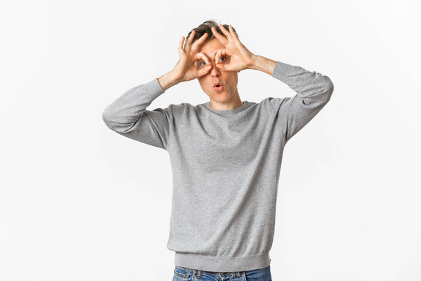 Портрет смішного хлопця середнього віку, який робить обличчя, показуючи окуляри рук навколо очей і обманюючи навколо, стоячи на білому тлі
 - Фото, зображення
