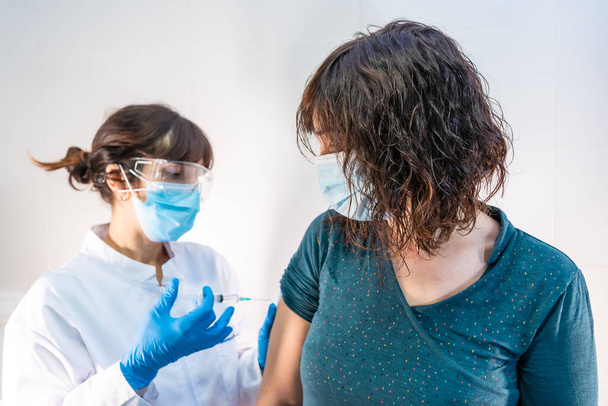 A female doctor with a face mask applying the coronavirus vaccine, the patient looking at the vaccine. First vaccines for people at risk, antibodies, new normal, covid-19. - Fotó, kép