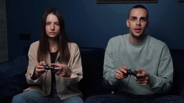 Heyecanlı çift evdeki TV karşısında kanepede otururken video oyunu oynuyor. Genç adam ve kadın boş zamanlarında joystickleri tutuyorlar.. - Video, Çekim