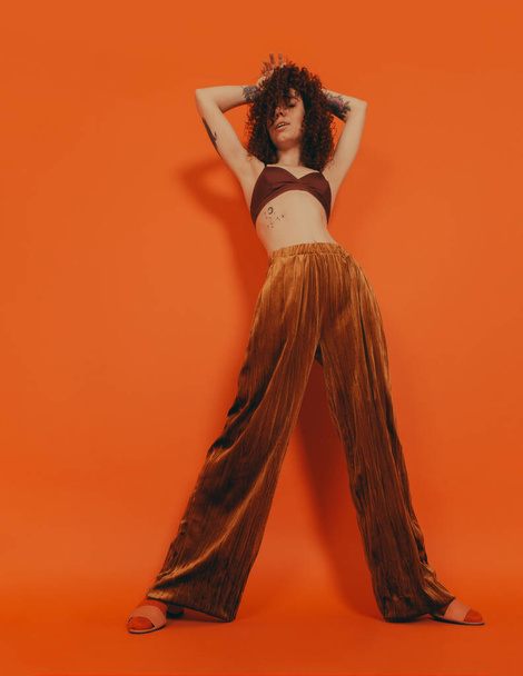 Pelirroja chica rizada en el estudio sobre un fondo naranja en ropa elegante - Foto, Imagen